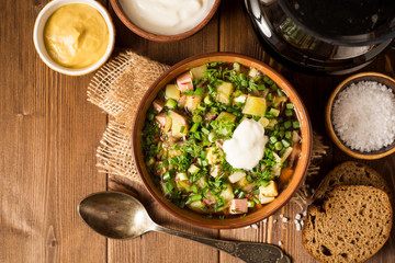Okroshka. Traditional Russian summer cold soup with sausage, vegetables and kvass in bowl on wooden background.