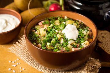 Okroshka. Traditional Russian summer cold soup with sausage, vegetables and kvass in bowl on wooden background.