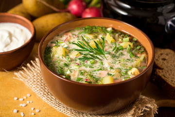 Okroshka. Traditional Russian summer cold soup with sausage, vegetables and kvass in bowl on wooden...