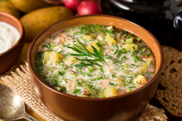 Okroshka. Traditional Russian summer cold soup with sausage, vegetables and kvass in bowl on wooden background.
