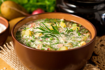 Okroshka. Traditional Russian summer cold soup with sausage, vegetables and kvass in bowl on wooden...