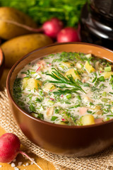 Okroshka. Traditional Russian summer cold soup with sausage, vegetables and kvass in bowl on wooden background.