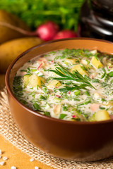 Okroshka. Traditional Russian summer cold soup with sausage, vegetables and kvass in bowl on wooden background.