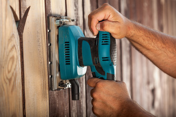 Worker hands using electric vibrating sander - closeup