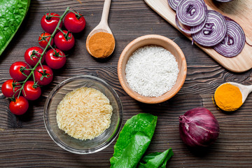 rice, spices and vegetables for paella on wooden desk background top view