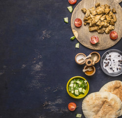Ingredients for cooking home-made shawarma, fried chicken with condiments, pita, sliced cucumbers, condiments and spices, on wooden rustic background boarder, place for text