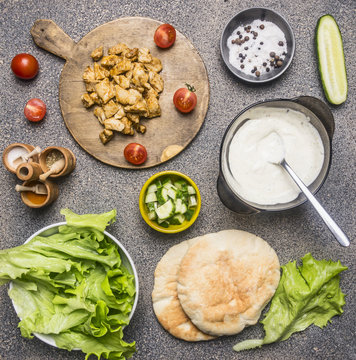 Ingredients for cooking home-made shawarma, fried chicken with condiments, pita, sliced cucumbers, condiments and spices, on wooden rustic background boarder, place for text