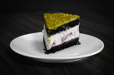 Berry and chocolate cake topped with pistachio served in white plate on wooden table