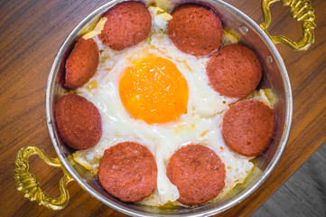Closeup of Turkish sausage (sucuk) and fried egg in a copper pan on wooden table