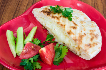 Closeup of Turkish toast (Tost), toasted sandwich with cheddar cheese served in red plate with vegetables on wooden table
