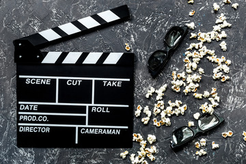 Watching the film. Movie clapperboard, sunglasses and popcorn on grey stone table background top...