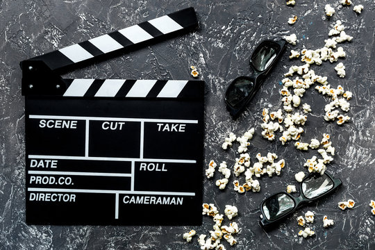 Watching the film. Movie clapperboard, sunglasses and popcorn on grey stone table background top view