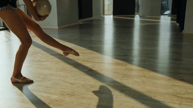 Legs of young girl training in gymnastics exercise with ball in the hands in the ballet studio on sunshine background. Close up.