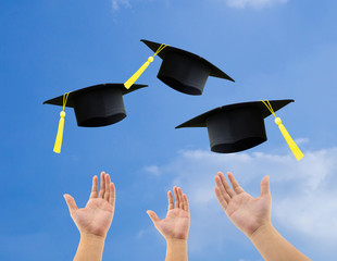 Students throwing graduation hats in the air celebrating on sky background