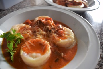 Upper detail view of two plates of sorrentinos - stuffed pasta - with sauce, parmesan cheese, and decorated with some parsley´s leaves