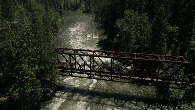 Lifestyle Aerial of Whitewater Kayaker Paddling Under Bridge Surrounded by Forest Trees in 4K 60P