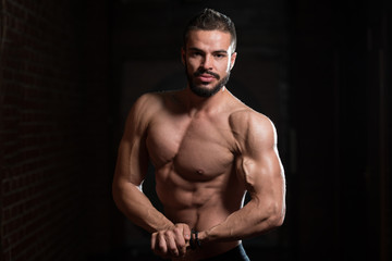 Fototapeta na wymiar Handsome Muscular Model Flexing Muscles In Gym