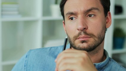 Portrait of attractive thoughtful business man holding the pen and writting something in the notebook. Close up.