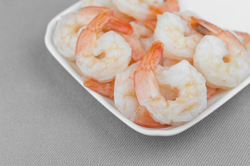 boiled shrimps in a white plate on grey cotton fabric background, close up