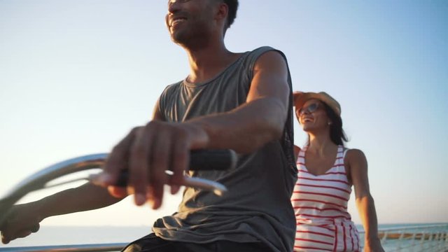 Portrait of a mixed race couple riding on tandem bicycle outdoors near the sea, slow motion