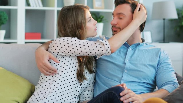 Young attractive woman gentle stroking the face on her boyfriend while they relaxing on the sofa at home.