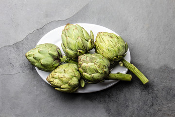Fototapeta premium Fresh artichokes on withe plate, slate background