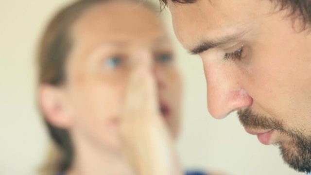 Woman whispers in the man's ear secret. He's angry. Profile of a man close-up. Woman's face is blurry