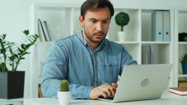 Young man working on the laptop in the office, filing so borring, dreaming about finish of work day.
