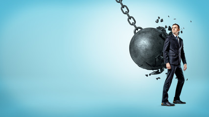 A businessman on blue background looking up over his shoulder white a wrecking ball crashes on his...