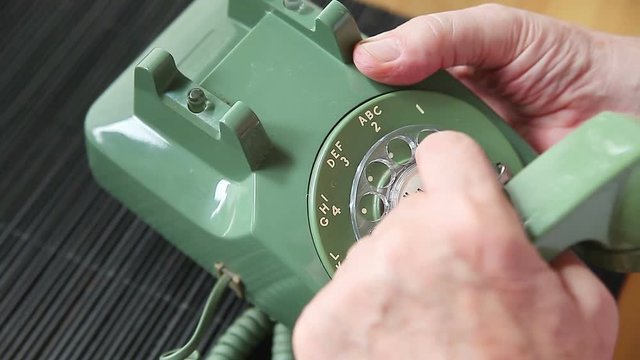 Man holds handset of old rotary phone while dialing with same hand