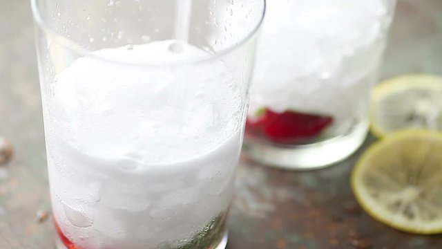 Adding carbonated water to glasses of strawberries, mint and crushed ice
