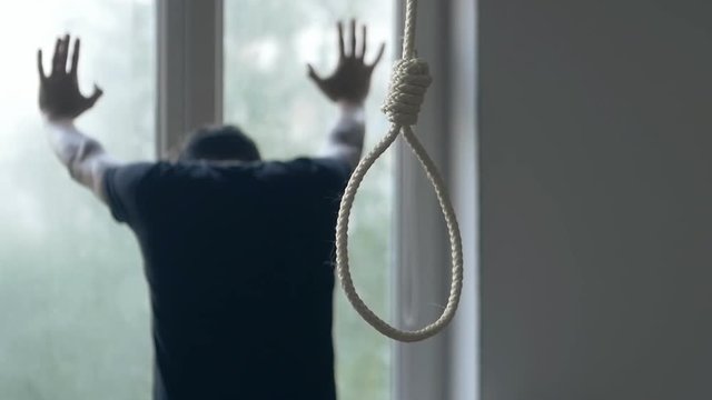 Suicide. Depressed man crying near window on the background of the loop for the neck.