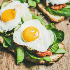 Healthy breakfast sandwiches. Bread toasts with fried eggs and fresh vegetables on rustic wooden board background, selective focus, square crop. Clean eating, healthy, diet, weight loss food concept