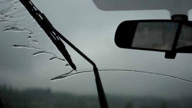 Slow motion of rainy day view during car windshield wipers rain drops sliding down inside a car