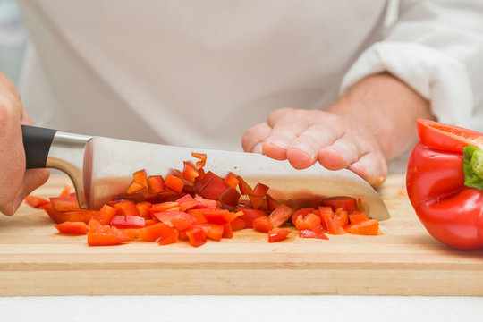 Chef's hands with knife cutting sweet paprika on the wooden board. Preparation for cooking. Healthy eating and lifestyle.