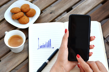 Woman browsing smartphone above table with coffee and cookies