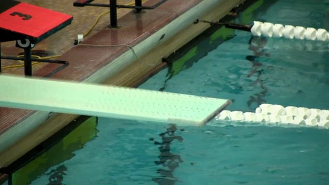 High school female diver stands at the edge of a diving board and springs herself off into a back dive during diving meet