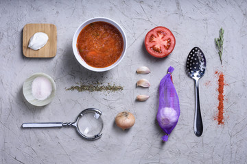 Cooking ingredients on grey background, tomato soup with herbs.