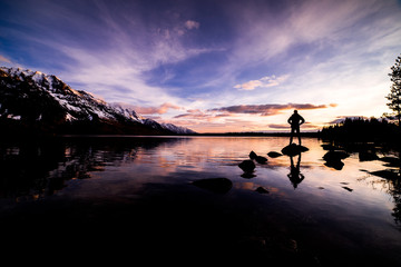 Sunrise on Jenny Lake with stunning colors and a person standing on a Rock Silhouetted