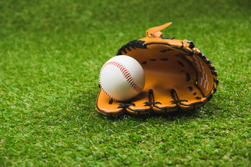 Close-up view of leather baseball glove and ball on green grass