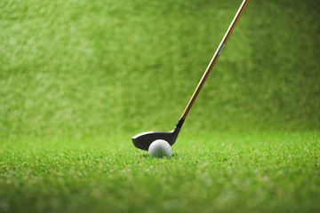Close-up view of golf club and white ball on green grass