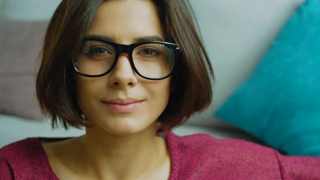 Portrait of caucasian young woman in glasses with short dark hair posing at the camera raising eyebrows at home.