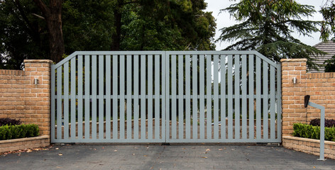 Metal driveway entrance gates set in brick fence trees in background