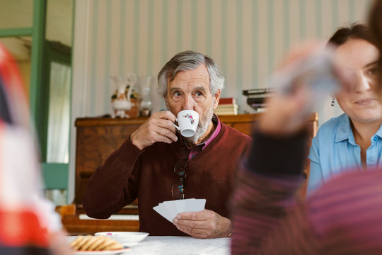 Senior man drinking coffee while playing cards with family at home