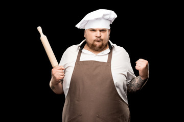 Naklejka premium Angry young chef holding rolling pin and shaking fist isolated on black
