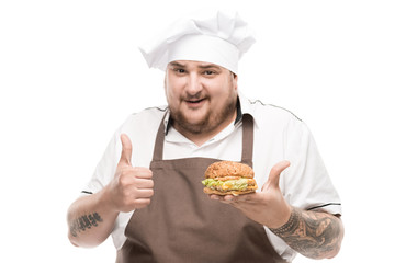 smiling cooker with burger in hand showing thumb up isolated on white
