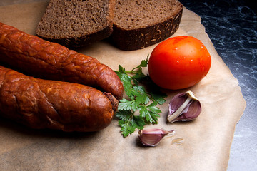 Close up view smoked sausage with spice, herbs and vegetables on the packaging paper.