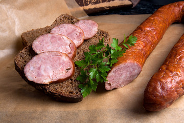 Slices of smoked sausage with spice, herbs and vegetables on the packaging paper.