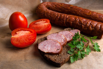 Slices of smoked sausage with spice, herbs and vegetables on the packaging paper.