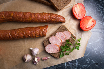 Slices of smoked sausage with spice, herbs and vegetables on the packaging paper.